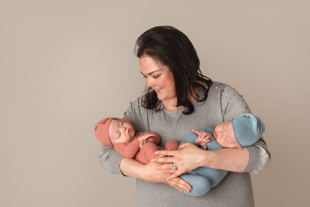mom looks down at babies in arms during studio newborn session 